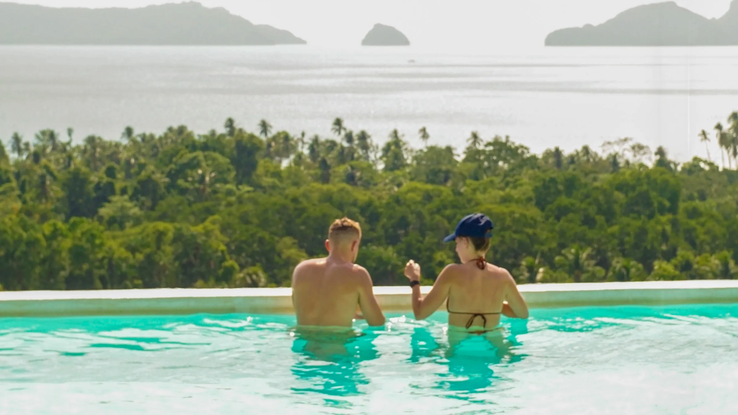 Two guests in the infinity pool looking out to the islands of Bacuit Bay
