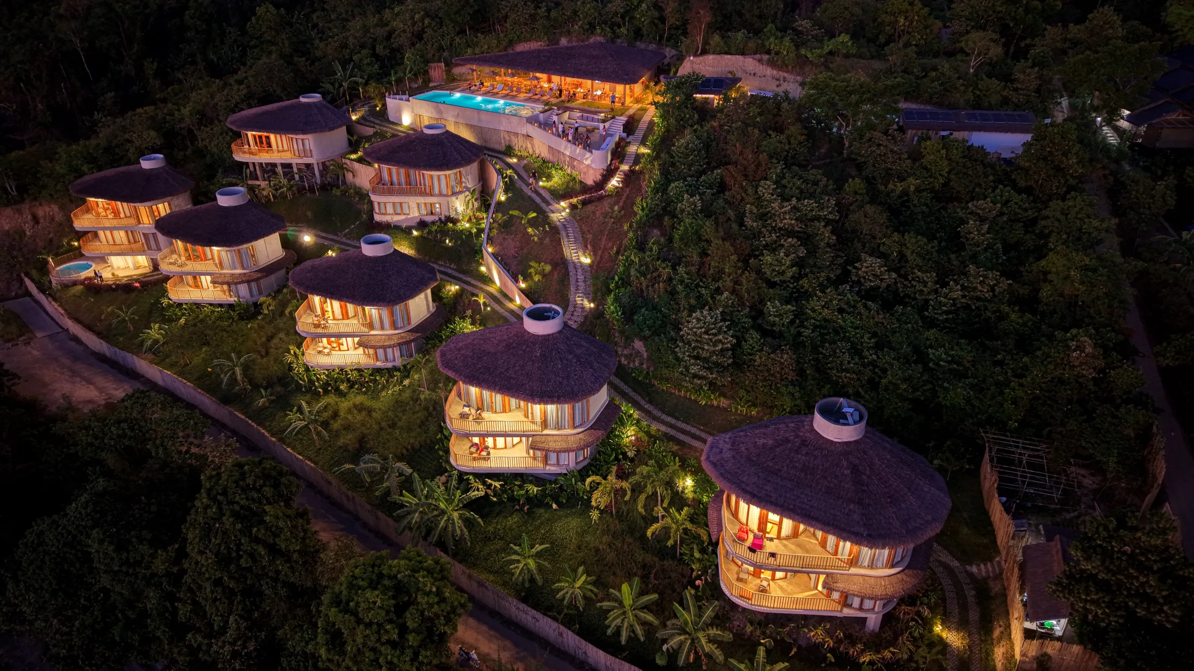 Aerial view of Atalaya Resort's thatched villas lit at dusk on the hillside above El Nido